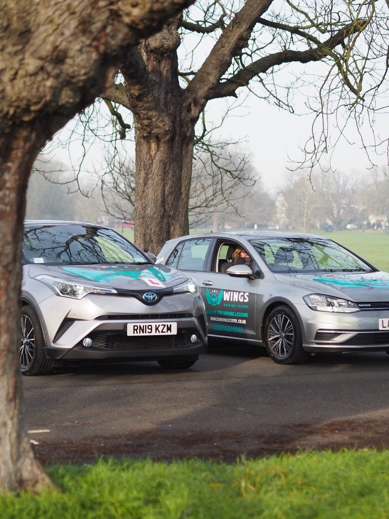 Two Wings Driving School cars parked by a park